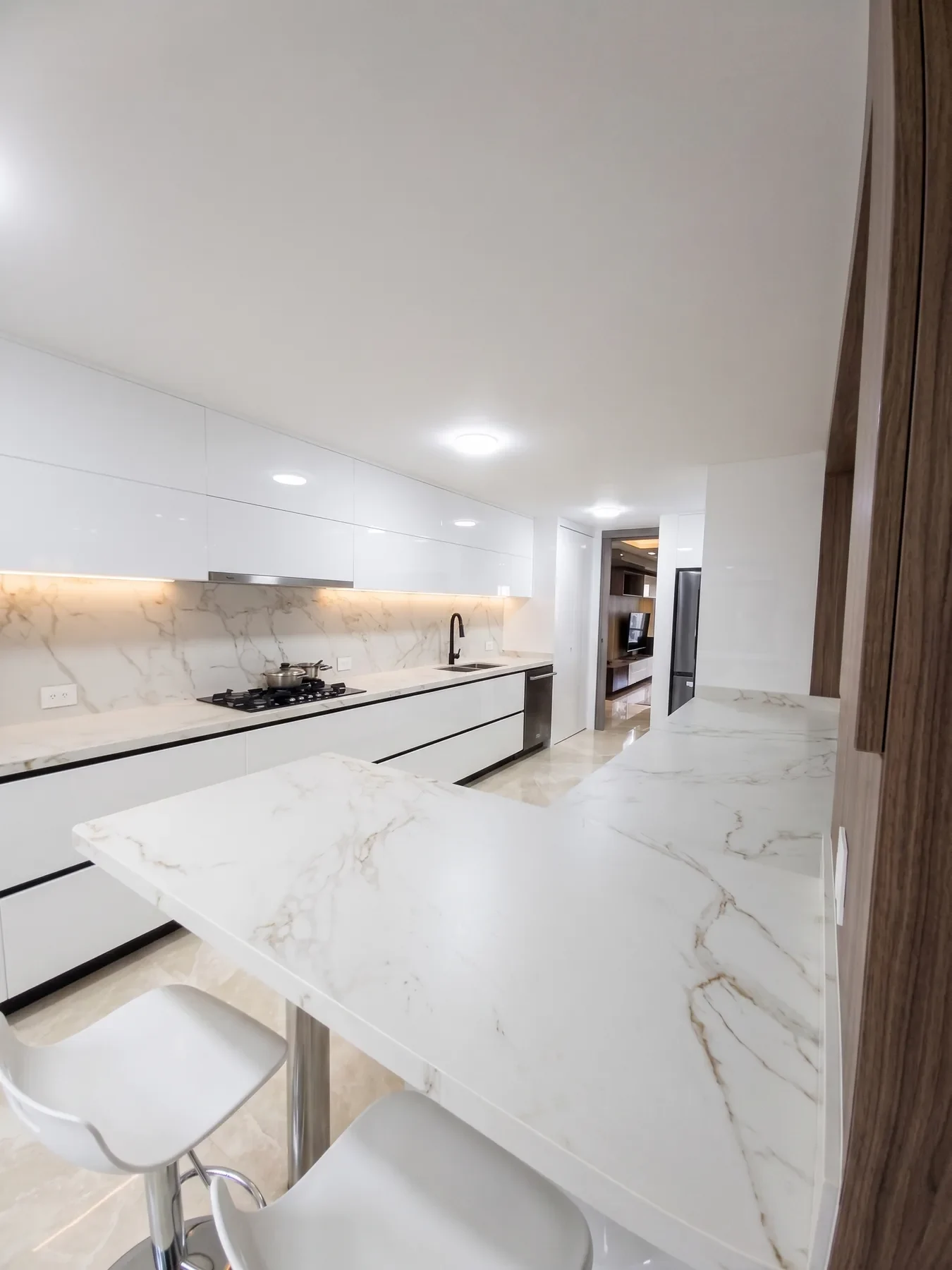 Cocina Montereserva terminada: gabinetes blancos de alto brillo, barra en piedra tipo mármol y butacos blancos
